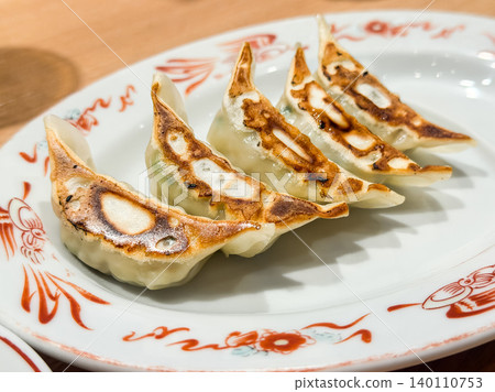 Five dumplings lined up on a plate. Fragrant pan-fried dumplings like you'd find at a ramen shop. The browned surface looks delicious. Five dumplings lined up on a plate. Fragrant pan-fried dumplings like you'd find at a ramen shop. The browned surface looks delicious. 140110753