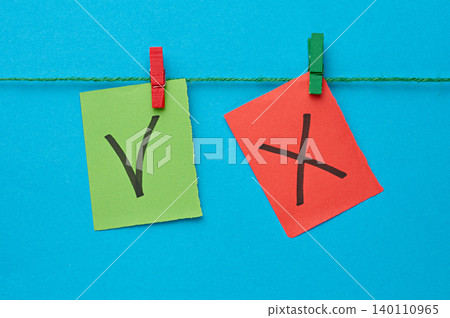 A green sticker with a check mark and a red sticker with a cross are attached to a string with wooden clothespins 140110965