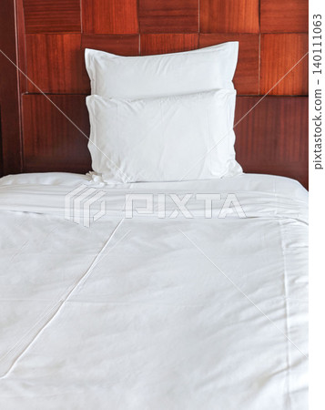 White bedding with a neatly arranged pillow on a wooden headboard in a modern bedroom setting, showcasing a clean and minimalist design aesthetic White bedding with a neatly arranged pillow on a wooden headboard in a modern bedroom setting, showcasing a clean and minimalist design aesthetic 140111063