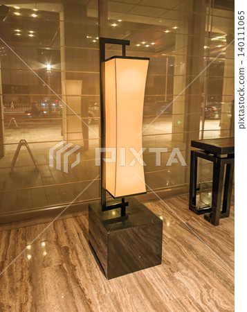 Modern floor lamp with a soft glow illuminating a marble floor in a contemporary lobby, featuring glass walls and reflections of city lights outside Modern floor lamp with a soft glow illuminating a marble floor in a contemporary lobby, featuring glass walls and reflections of city lights outside 140111065