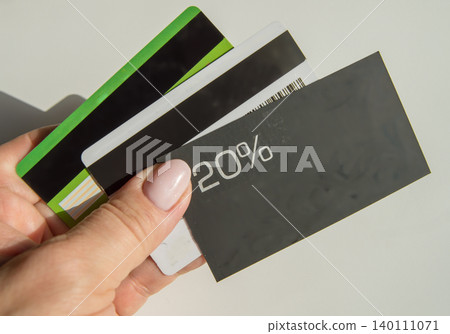 A man's hand holding a discount card with a 20 percent discount and a copy of the place and several plastic bank cards, the concept of saving finances A man's hand holding a discount card with a 20 percent discount and a copy of the place and several plastic bank cards, the concept of saving finances 140111071