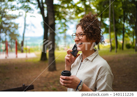 Woman smiling while talking on phone and holding coffee in park 140111226