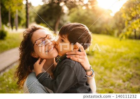 Mother giving son a loving kiss outdoors Mother giving son a loving kiss outdoors 140111232