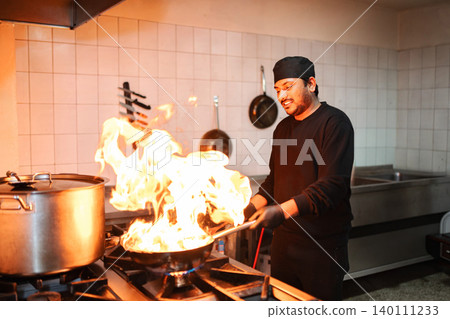 Male chef flambe cooking food in a pan on a stove Male chef flambe cooking food in a pan on a stove 140111233
