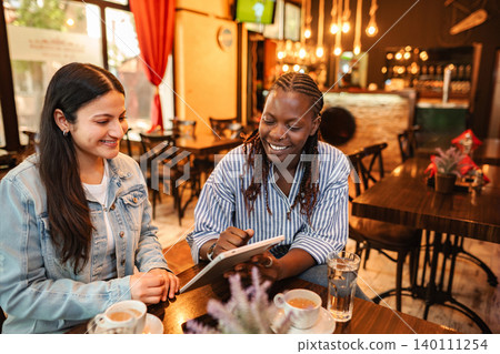 Diverse friends connecting and smiling using digital tablet in cafe 140111254