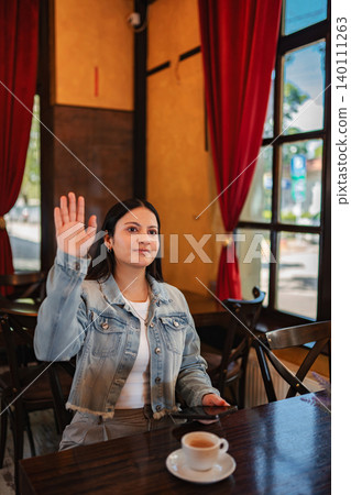 Young adult woman raising hand calling waiter in cafe Young adult woman raising hand calling waiter in cafe 140111263