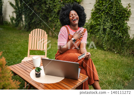 African American woman laughing buying online with laptop and credit card African American woman laughing buying online with laptop and credit card 140111272