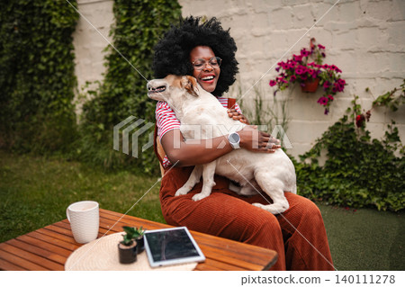 Happy black woman hugging pet dog in backyard Happy black woman hugging pet dog in backyard 140111278