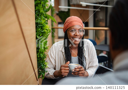 Black woman smiling during coffee meeting in coworking space Black woman smiling during coffee meeting in coworking space 140111325