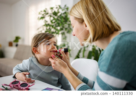 Mother applying lipstick to daughter learning makeup at home 140111330