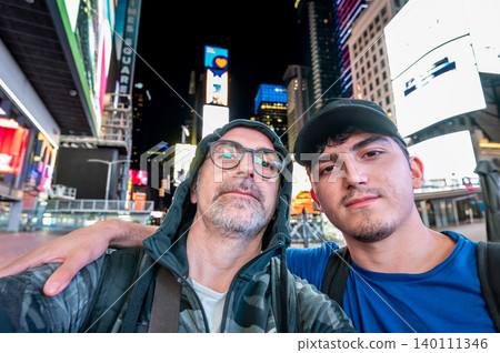 New york, usa august 21,2024. Father and son tourists smiling for a selfie amid times squares bright neon billboards and bustling manhattan nightlife, bonding together 140111346