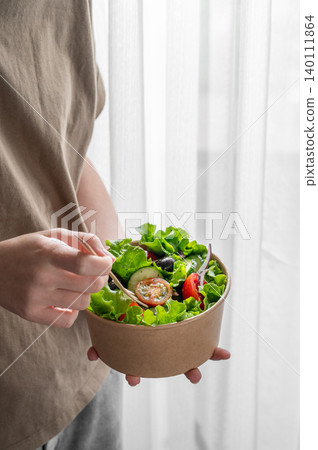 A woman holds a healthy vegetable salad in an eco-friendly takeaway bowl. A woman holds a healthy vegetable salad in an eco-friendly takeaway bowl. 140111864