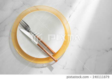 A white and yellow plates with a fork, knife on a marble background A white and yellow plates with a fork, knife on a marble background 140111879