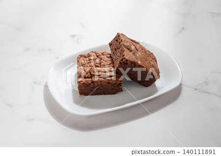 A pieces of chocolate brownie on a white plate on a marble background A pieces of chocolate brownie on a white plate on a marble background 140111891