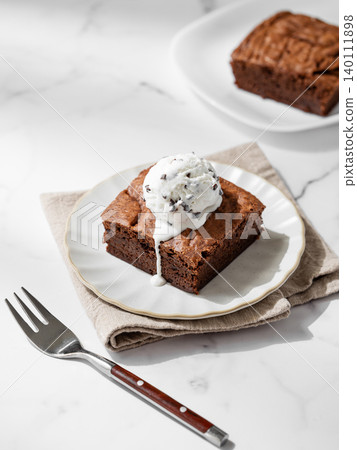 A pieces of chocolate brownie with ice cream on a plate on a light marble background A pieces of chocolate brownie with ice cream on a plate on a light marble background 140111898