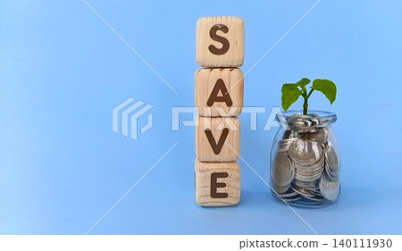 Coins in a glass with a growing plant and a wooden cube that says "save." The concept of saving. Coins in a glass with a growing plant and a wooden cube that says "save." The concept of saving. 140111930