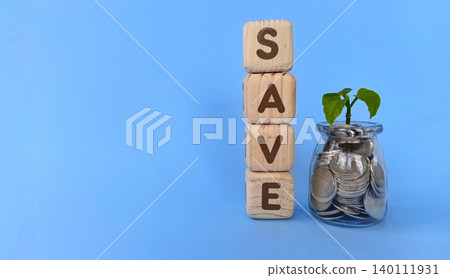 Coins in a glass with a growing plant and a wooden cube that says "save." The concept of saving. Coins in a glass with a growing plant and a wooden cube that says "save." The concept of saving. 140111931