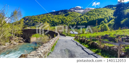 Scenic view of a winding road leading to a stone bridge over a river in the Pyrenees mountains with lush greenery and blue sky Scenic view of a winding road leading to a stone bridge over a river in the Pyrenees mountains with lush greenery and blue sky 140112053