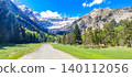Scenic view of the Pyrenees mountains with snow-capped peaks, lush green valley, and hiking trail under a clear blue sky 140112056