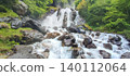 Waterfall cascading over large rocks surrounded by lush greenery in the Pyrenees mountains, creating a serene natural landscape 140112064
