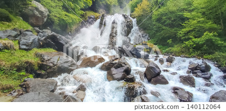 Waterfall cascading over large rocks surrounded by lush greenery in the Pyrenees mountains, creating a serene natural landscape 140112064