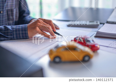 A man signing a contract for a car loan, lease, vehicle registration or insurance policy. Concept for Sales Contract, Financing Agreement, Insurance Policy, Vehicle Registration. A man signing a contract for a car loan, lease, vehicle registration or insurance policy. Concept for Sales Contract, Financing Agreement, Insurance Policy, Vehicle Registration. 140112371