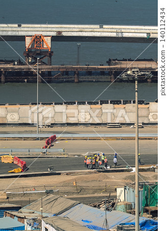 An elevated view showing ongoing construction work on a new coastal road or bridge project in Mumbai, with heavy machinery and materials visible 140112434