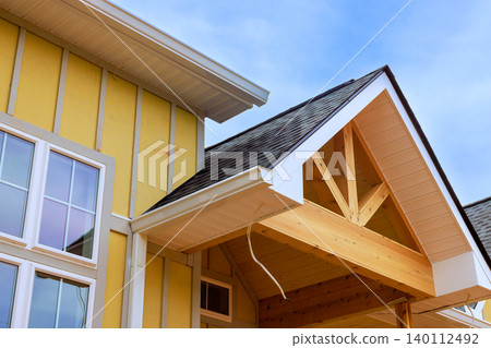 House is being built with yellow siding roof made of wooden beams construction is in progress. 140112492