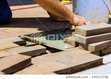 Worker is carefully placing bricks on surface while using trowel to apply mortar 140112506