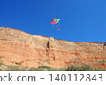Bright colorful kite flying high above sunlit canyon cliff on a clear summer day. Travel and nature, family vacations, childhood memories, summer leisure, festivals, ecotourism, freedom and lightness 140112843