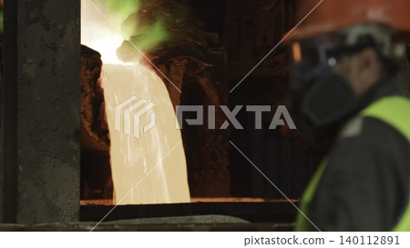 Worker Wearing Safety Equipment Observes Glowing Molten Metal During Industrial Smelting Operation. Stock Clip Worker Wearing Safety Equipment Observes Glowing Molten Metal During Industrial Smelting Operation. Stock Clip 140112891