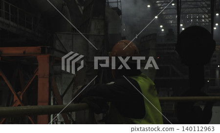 Diligent Shift Leader Wearing Protective Gear Overseeing Manufacturing Process Amid Industrial Environment . Stock clip 140112963