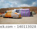 Improvised colorful camping setup with car covered in tarp at dry summer hillside campsite. Camping, festivals, alternative travel, sustainable tourism, outdoor life, survival, vanlife, boho adventure 140113028