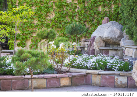 Tranquil backyard garden with rock bench, white flower bed and ivy-covered wall Tranquil backyard garden with rock bench, white flower bed and ivy-covered wall 140113117