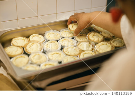 Middle aged Black woman hand arranging handmade tarts in metal tray inside commercial kitchen Middle aged Black woman hand arranging handmade tarts in metal tray inside commercial kitchen 140113199
