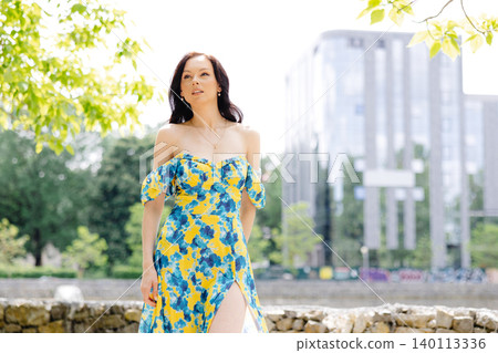 Young woman in summer dress is walking in green park and enjoying the sun. Playful and beautiful girl on warm sunny day. Young woman in summer dress is walking in green park and enjoying the sun. Playful and beautiful girl on warm sunny day. 140113336