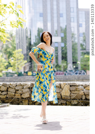 Young woman in summer dress is walking in green park and enjoying the sun. Playful and beautiful girl on warm sunny day. 140113339