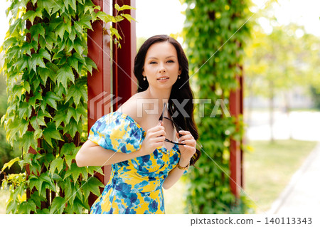 Beautiful young woman with long hair in trendy summer dress and sun glasses is walking in the park Beautiful young woman with long hair in trendy summer dress and sun glasses is walking in the park 140113343