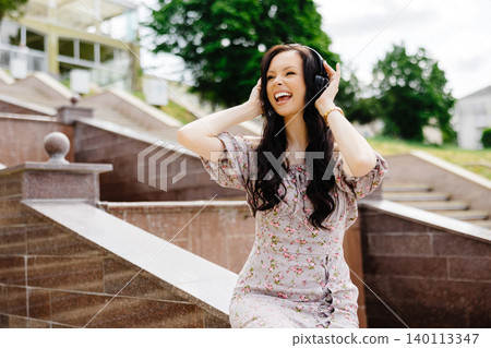 Dancing girl feeling happy in city.Young woman dancing and listening music in headphones, standing on the stairs in park Dancing girl feeling happy in city.Young woman dancing and listening music in headphones, standing on the stairs in park 140113347