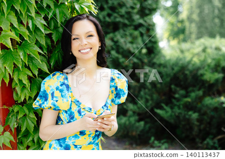 Portrait of a beautiful young woman standing at the green leaves tree Portrait of a beautiful young woman standing at the green leaves tree 140113437