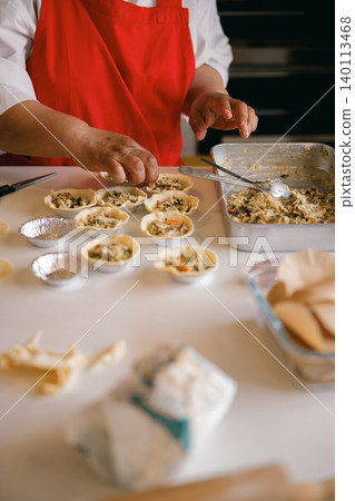 Senior Latina Woman Preparing Savory Mini Pastries in a Bright Domestic Kitchen Workshop Senior Latina Woman Preparing Savory Mini Pastries in a Bright Domestic Kitchen Workshop 140113468