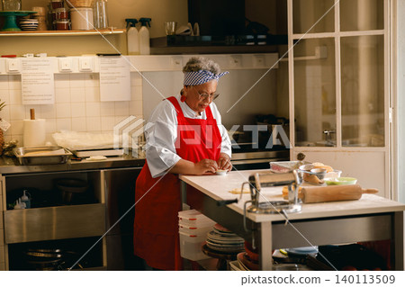 Senior Black woman pastry chef preparing dough in a professional commercial kitchen bakery workshop Senior Black woman pastry chef preparing dough in a professional commercial kitchen bakery workshop 140113509