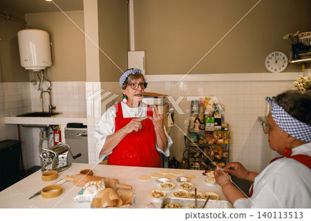 Elderly Caucasian woman teaching a cooking class and preparing tarts in a commercial kitchen Elderly Caucasian woman teaching a cooking class and preparing tarts in a commercial kitchen 140113513