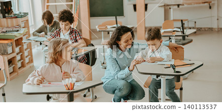 Hispanic female teacher helping young diverse elementary school students in a bright classroom Hispanic female teacher helping young diverse elementary school students in a bright classroom 140113537