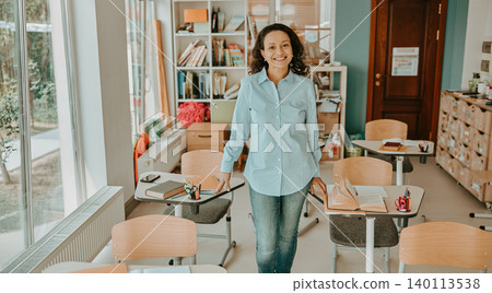 Mature Hispanic female teacher standing and smiling in a bright modern school classroom Mature Hispanic female teacher standing and smiling in a bright modern school classroom 140113538