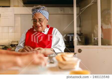 Senior Black woman chef preparing food in professional kitchen showcasing active longevity 140113540