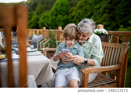 Little boy with his grandmother looking in smartphone during bbq party. Little boy with his grandmother looking in smartphone during bbq party. 140113573