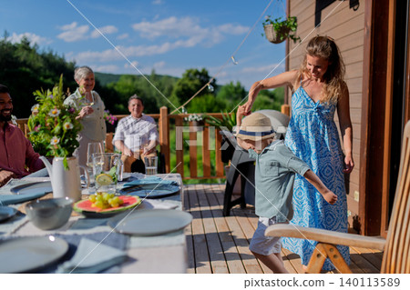 Family with kids having fun at barbecue party dinner on patio, people sitting at table on patio and talking Family with kids having fun at barbecue party dinner on patio, people sitting at table on patio and talking 140113589