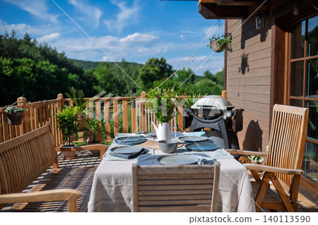 Outdoor barbecue setup on wooden terrace with dining table and grill. Outdoor barbecue setup on wooden terrace with dining table and grill. 140113590