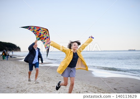 Senior man and his preteen granddaughter preparing kite for flying on sandy beach. 140113629